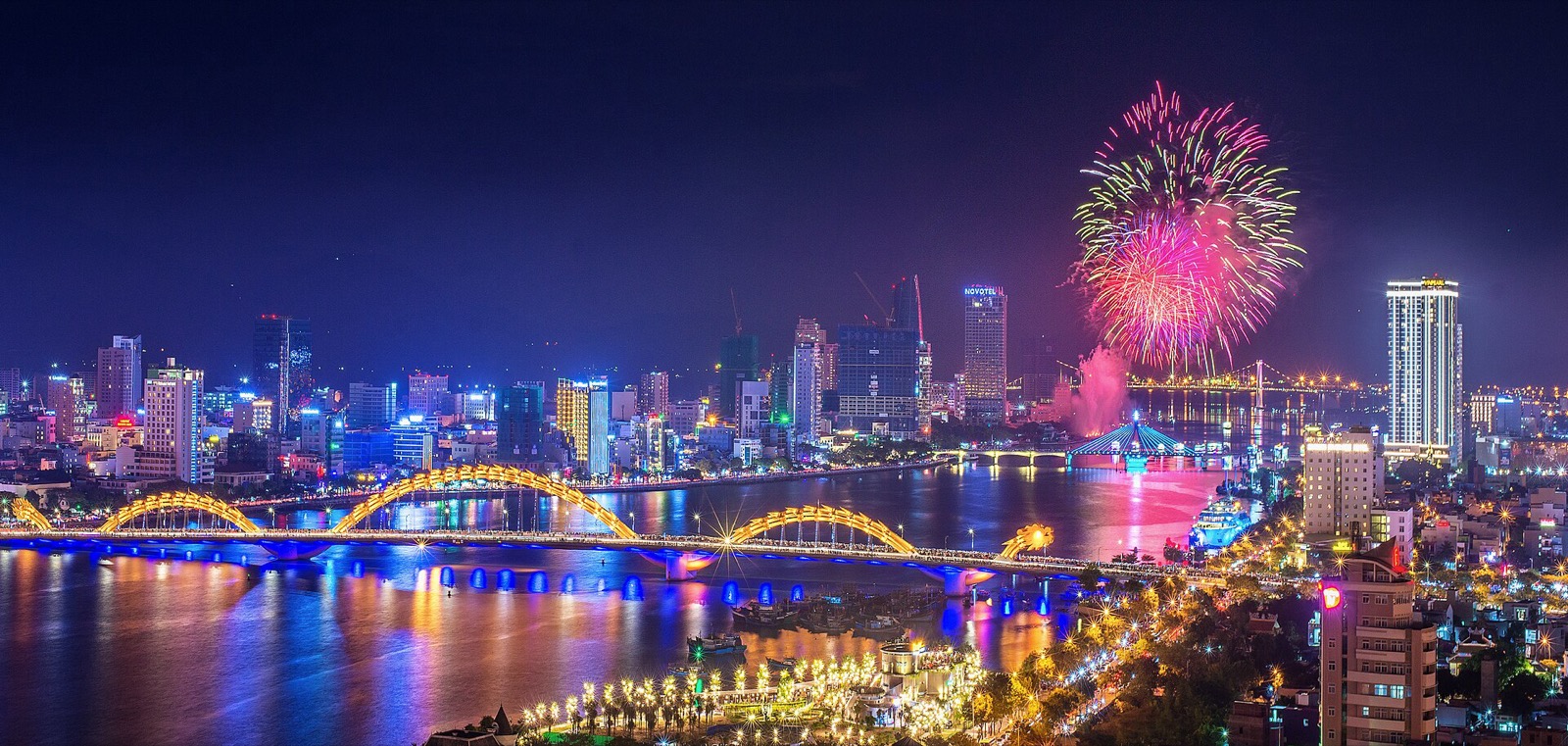 Фейерверк над рекой Хан ночью во время фестиваля в Дананге, на переднем плане подсвеченный мост Дракона, за рекой высотки